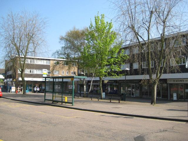 The local shopping parade at Carpenders Park, flats above the shops and a bus shelter on the wide pavement in front