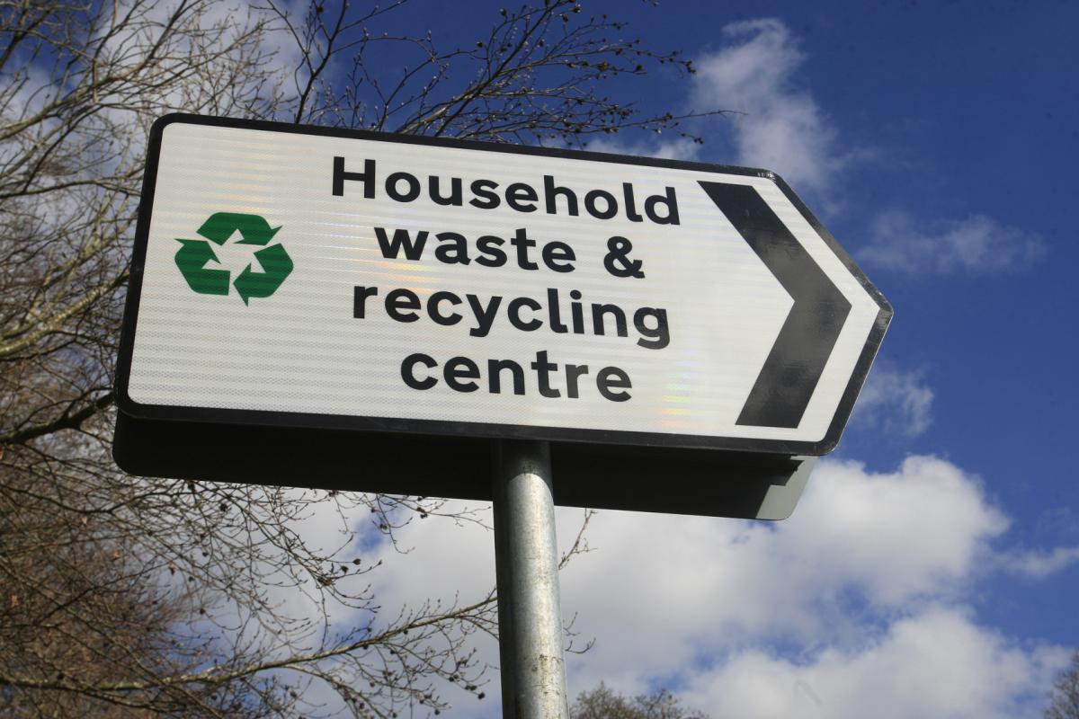 A roadside sign pointing the way to a household waste and recycling centre against a blue sky