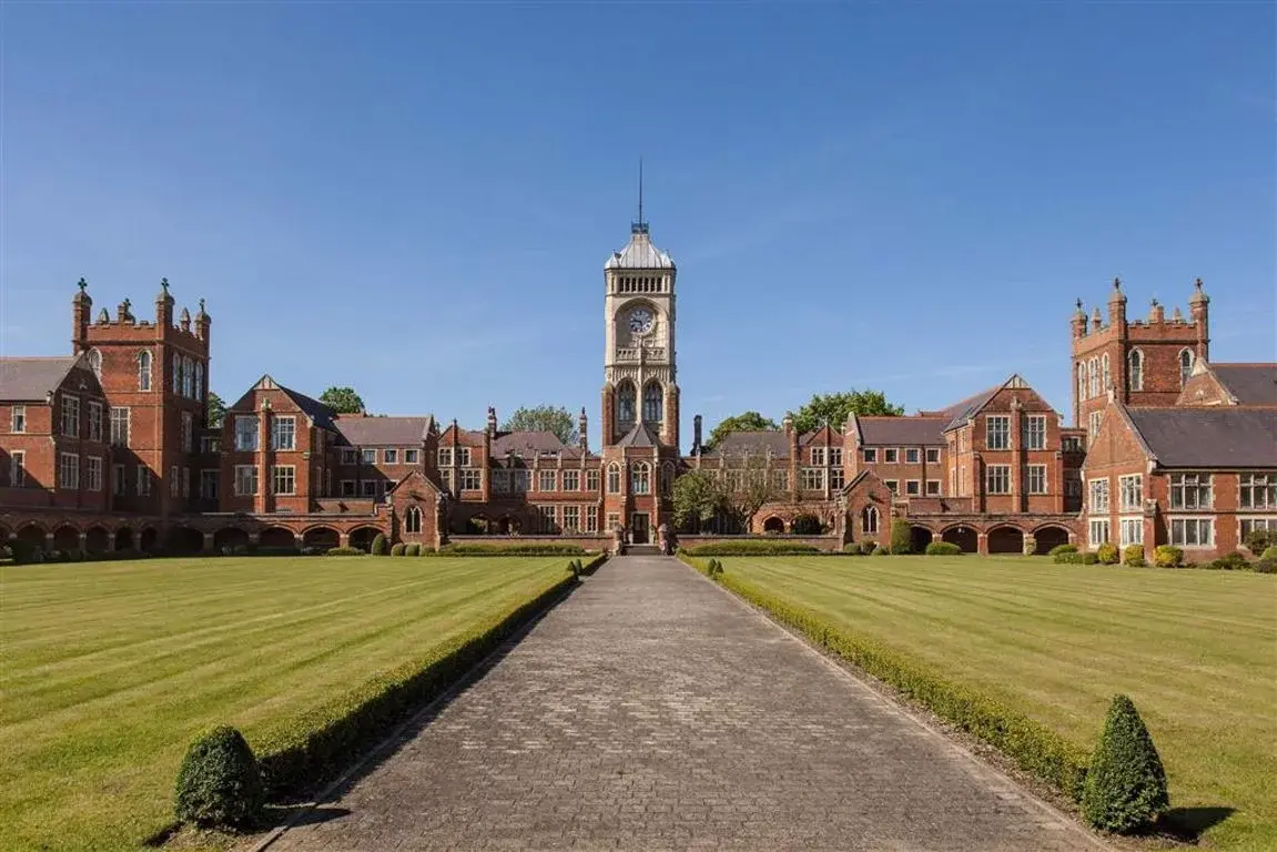 A large Victorian red-brick building with a central clock tower in Bushey, seen from the far end of a paved avenue between formal lawns