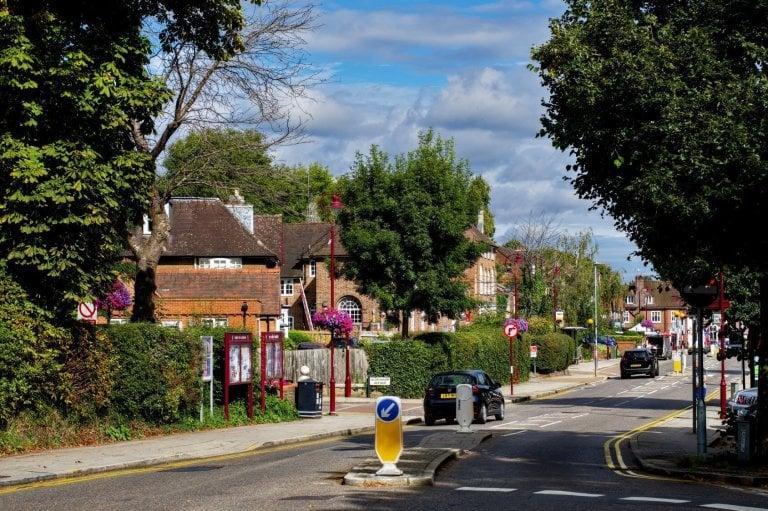 Watling Street running through the centre of Radlett, red-brick buildings set back behind clipped hedges and cars parked along the kerb